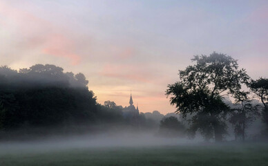 Colorful glowing sunrise with mist over a countryside meadow area around a distant castle, creating an idyllic scenic landscape