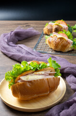 Delicious croissants sandwichs with fresh Ham, cheese, tomato, cucumber, lettuce served on sieve and Sub sandwich with fresh salad, Ham , cheese served on round wooden plate. wooden background.