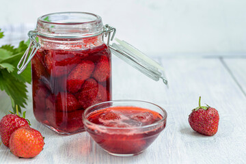 Strawberry jam in a glass jar next to fresh strawberries. On a white wooden background. Homemade winter fruit blanks. Selective focus.