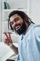 Handsome young African man smiling and looking at camera while taking selfie indoors