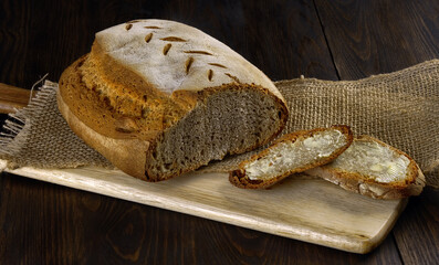 Fresh baked loaf of sourdough bread and two slices of bread with butter on wooden board and jute over wooden table