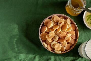 Bowl with tiny pancake cereal porridge on a green textile background top view with copy space.Trendy tasty breakfast food