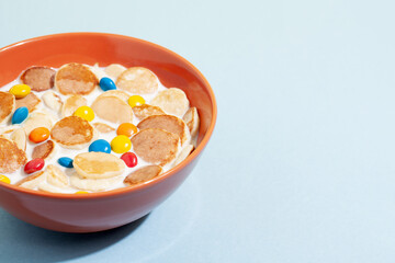 Orange bowl with tiny pancake cereal porridge with milk on a blue background.Trendy tasty breakfast food