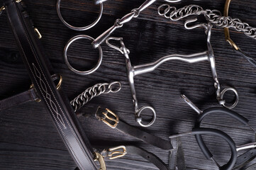  various bits  with mouthbridle and spurs on black wooden  background. flat lay