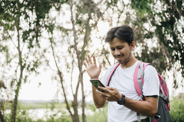 Young Asian man traveling backpacker video calling in the forest, Concept of nature tourism