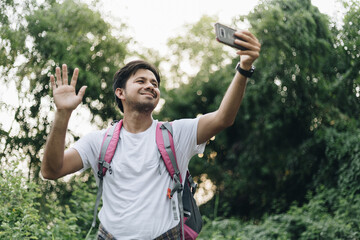 Young Asian man traveling backpacker video calling in the forest, Concept of nature tourism