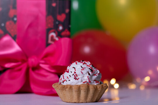 festive cupcake on the background of red gift box with a pink ribbon, multi-colored balloons and lights. party, birthday concept. Copy space. . High quality photo