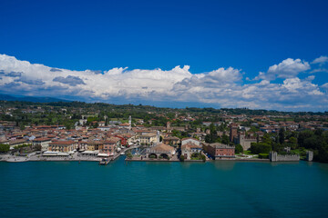 Fototapeta premium Lazise, Jezioro Garda, Włochy. Widok z lotu ptaka na zabytkową część zamku Scaliger w Lazise w tle chmury cumulus na niebieskim niebie