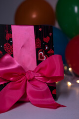 A red gift box with a pink ribbon on a background of multi-colored balloons and lights. party, birthday concept. Copy space. High quality photo