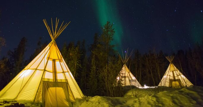 Lockdown time lapse shot of illuminated tents on snow by trees against sky at night - Northwest Territories, Canada