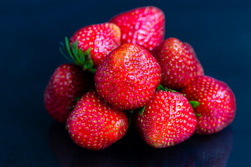 Large ripe strawberries are collected from the garden. On a black wooden background. Homemade winter fruit blanks. Selective focus.