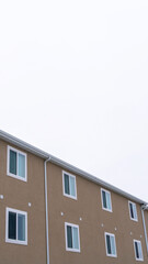 Vertical frame Back view of townhouses with snowy roofs against overcast sky in winter