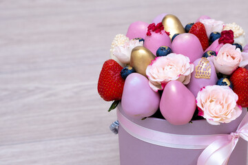 Fresh strawberries in pink, gold and white chocolate with pink flowers in the form of a fruit bouquet.