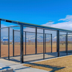 Square Baseball field dugout with slanted roof and chain link fence on a sunny day