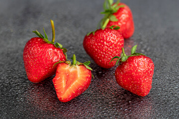 Large ripe strawberries are collected from the garden. On a black wooden background. Homemade winter fruit blanks. Selective focus.