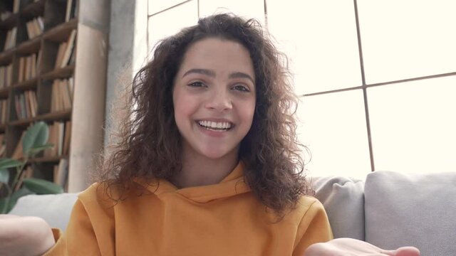 Happy hispanic latin gen z teen girl blogger content maker smiling face wearing hoodie waving hand talking to cam online followers recording live vlog video blog, social media channel stream at home.