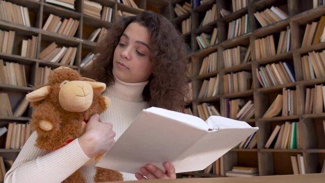 Young latin hispanic woman remote teacher reading fairy tale book teaching online sitting at library desk holding book toy looking at webcam. Remote children virtual video call zoom education concept.