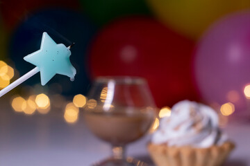 cupcake with a blue star-shaped candle and a glass with a brown liquid - liquer. On the background of multi-colored balloons and lights. party, birthday concept. Copy space. . High quality photo