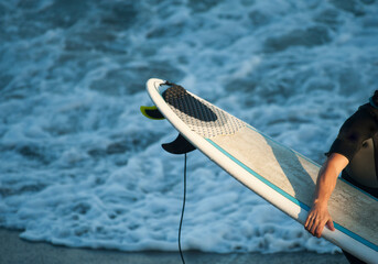 surfer man with surfboard in hand walking along the shore of the beach, surfboard on the beach at...