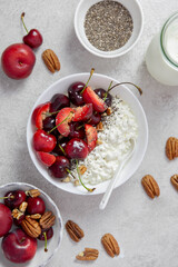 Cottage cheese with fresh cherry berries, plums, nuts, chia seeds and milk. In a white bowl on a light background. Top view.
