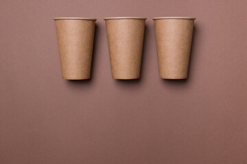 Three eco-friendly cardboard cups lie on a brown color paper background with copy space. Mock-up. Close-up. The concept of ecology