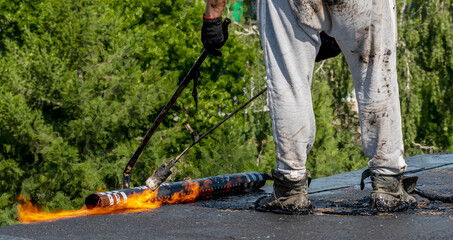 Overhaul of the roof of a living house. A construction worker using a gas burner puts waterproofing material. Fire in the frame.