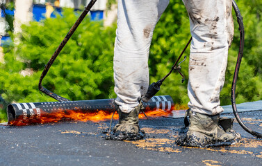 Obraz premium Overhaul of the roof of a living house. A construction worker using a gas burner puts waterproofing material. Fire in the frame.