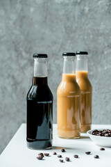 selective focus of cold brew coffee in bottles near coffee beans on white table