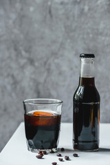 cold brew coffee with ice in glass and bottle near coffee beans on white table
