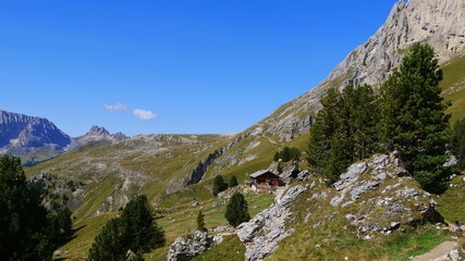 Bergpanorama mit Kiefern, Felsen und einer bewirtschafteten Hütte und Wanderweg