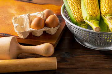 Corn cobs in colander on wooden background.
