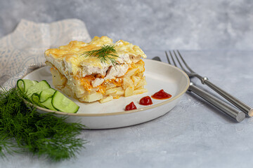 Potato casserole with chicken breast, carrots and onions. Topped with cheese. Garnished with fresh vegetables. but a gray background.