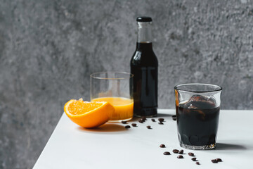 selective focus of cold brew coffee with ice in glass and bottle near orange juice and coffee beans on white table