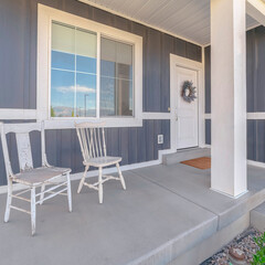 Square crop White porch chairs against window and front door of home with gray exterior wall