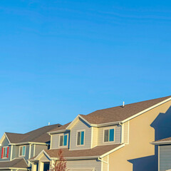 Square frame Homes with horizontal wall sidings and front gable roofs againts clear blue sky