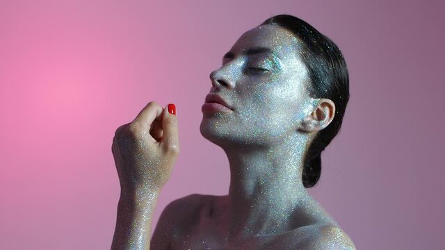 Slow motion video of a girl model with pouting lips with makeup from sparkles and glitters, posing in varying colors.