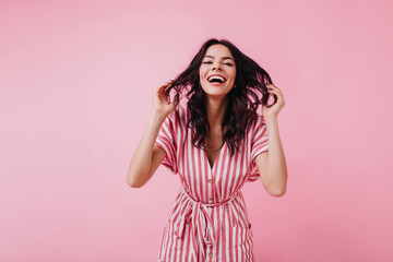 Blithesome caucasian lady playing with her wavy hair on pink background. Ecstatic slim woman having fun in studio