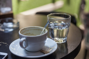 Close up on an Empty and dirty stained white porcelain coffee cup on display in the morning on the table of a cafe with a glass of water in the background.