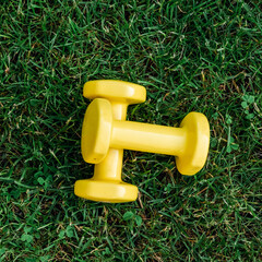 Set of two yellow dumbbells on a green grass background, top view. Staying in shape. Fitness and shape. Female exercise gear. Сoncept of outdoor fitness, nobody. Digital detox.