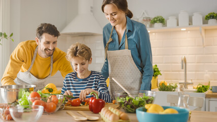 In Kitchen: Family of Three Cooking Together Healthy Dinner. Mother and Fathe Teach Little Boy Healthy Habits and to Cut Vegetables for Dinner Salad. Cute Child Helping their Beautiful Caring Parents