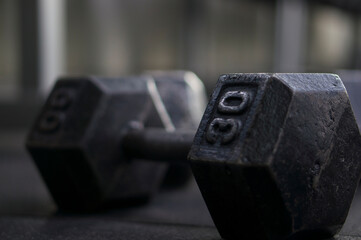 One black dumbbell on the black floor in the fitness room. Sport, fitness, weightlifting, healthy lifestyle. Exercise in the fitness room.