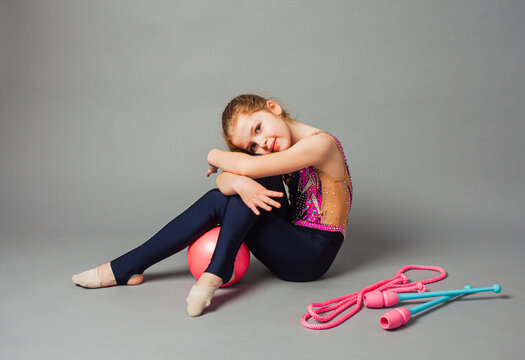 Girl gymnast posing with mace and rope on grey background.