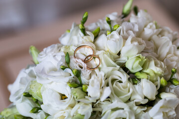 
Wedding rings in red gold on a bride’s bouquet of white roses and white azaleas, shot close-up from a high angle.
