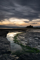 Bamburgh Castle on the northeast coast of England, by the village of Bamburgh in Northumberland. Moody and dramatic coastal image with imposing dark skies. Taken just after sunrise..