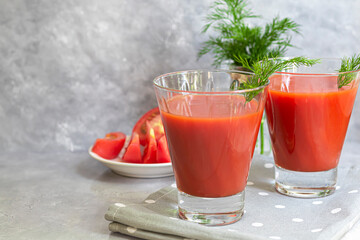 Tomato juice in glass cups and fresh tomatoes. On a light gray background. Vitamin drink. Garnished with sprigs of dill and coarse salt.