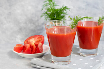 Tomato juice in glass cups and fresh tomatoes. On a light gray background. Vitamin drink. Garnished with sprigs of dill and coarse salt.