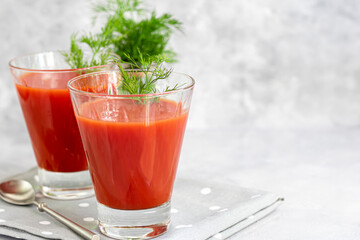 Tomato juice in glass cups and fresh tomatoes. On a light gray background. Vitamin drink. Garnished with sprigs of dill and coarse salt.