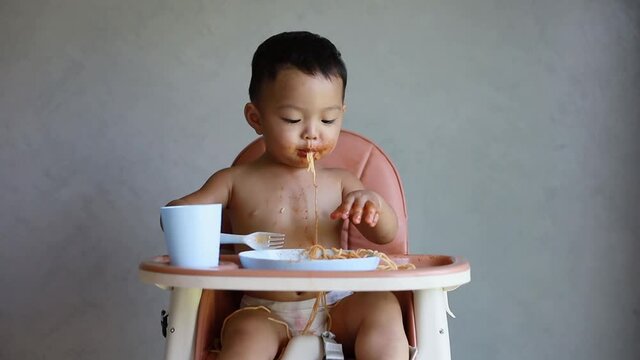 Asian boy eatting on high baby chair.