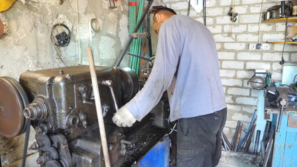 Adult man working with old workbench in his garage or workshop. Mechanic using lathe for metal processing. View on turning work. Slow motion Dolly shot