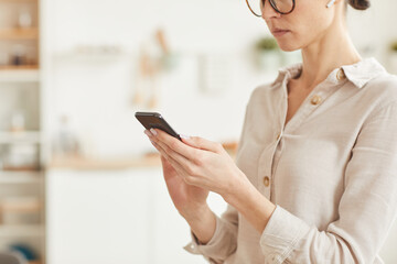 Warm-toned mid section portrait of elegant businesswoman using smartphone while standing in cozy home interior, copy space